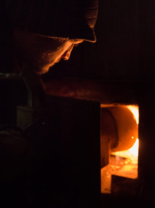Notre maître brasseur et distillateur entrouvre une trappe laissant apparaître le feu de bois pour notre distillation à chauffe directe.